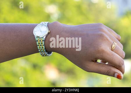 Una bella mano femminile con un orologio al polso, su uno sfondo verde sfocato. Indossa anche un anello d'oro al dito, simbolo del matrimonio. Foto Stock