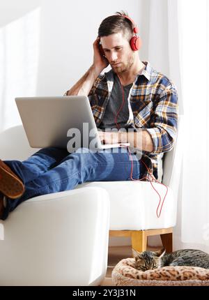 Uomo, serio e gatto su un laptop con cuffie per l'editing di video come videografo con lavoro in remoto. Persona maschile, animale domestico e concentrazione come libero professionista Foto Stock