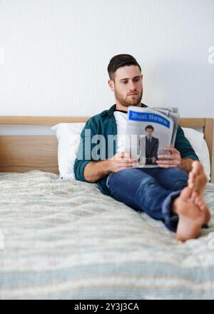 Uomo, relax e quotidiano a casa per leggere, aggiornamento aziendale e conoscenza sociale a letto. Persona, calmo e articolo sulla stampa per notizie aziendali Foto Stock