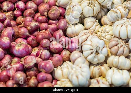 Vista ravvicinata dell'aglio fresco e delle cipolle rosse ammassate insieme. L'aglio ha un colore bianco cremoso con spicchi distinti, mentre le cipolle rosse sono piccole Foto Stock