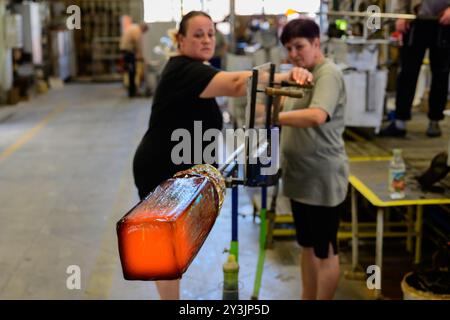 Karlovy Vary, Repubblica Ceca - 12 agosto 2024: Vaso di vetro Bohemian caldo nel processo di produzione tenuto da due lavoratrici al Moser Glass Foto Stock