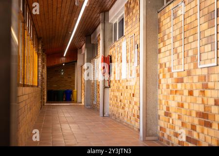 Corridoio scolastico vuoto con pareti in mattoni ed estintori, che portano alle aule Foto Stock