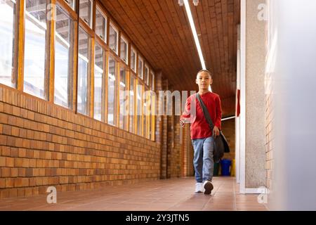 Camminando nel corridoio della scuola, portando un bambino con sé una borsa e indossando una camicia rossa Foto Stock