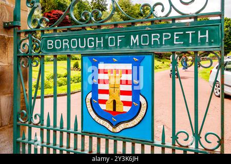 Cancello in ferro battuto con l'emblema Borough di Morpeth con un castello e strisce rosse e bianche situato nel giardino paesaggistico di northumberland Foto Stock