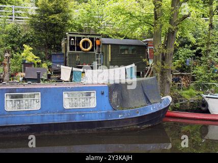 Un'antica barca blu sgarbata ormeggiata accanto a capannoni di legno con lavaggio sulla linea sul canale rochdale vicino al ponte hebden Foto Stock