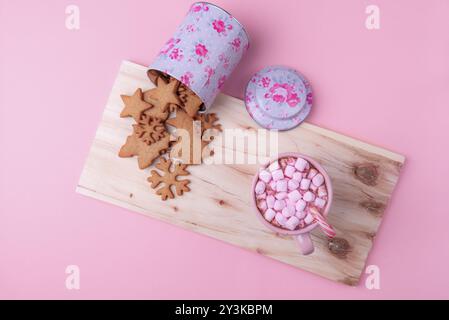 Natale minimalista, una tazza di cioccolata calda con mini marshmallow e canna da zucchero, una scatola rovesciata con biscotti al pan di zenzero su un piatto di legno Foto Stock