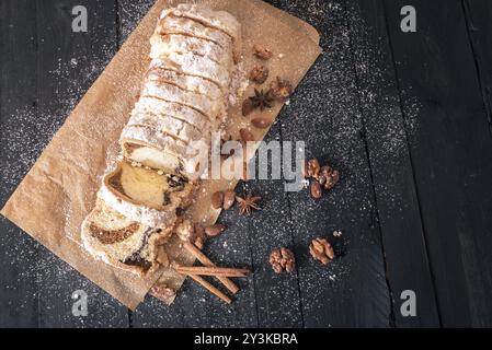 Vista al di sopra di una casalinga a fette di pan di spagna, riempito con dadi e semi di papavero, sulla sua carta da forno, coperto di zucchero a velo su una tavola in legno rustico Foto Stock