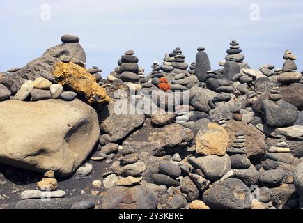 Primo piano di torri di ciottoli impilati e pietre colorate in una grande disposizione su una spiaggia di sabbia nera con cielo blu Foto Stock