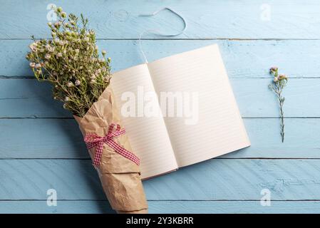 Bouquet di fiori bianchi e di agenda aperta su un blu tavolo in legno, piano immagine di laici Foto Stock