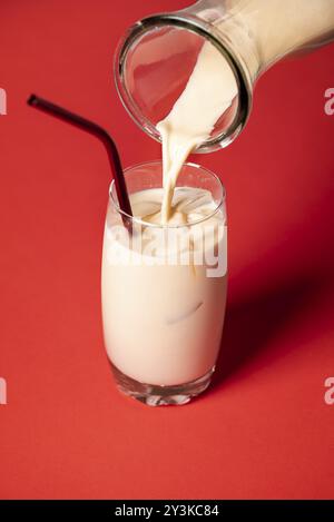 Versare horchata, mandorle messicane e latte di riso, in un bicchiere con cubetti di ghiaccio, su sfondo rosso. Serve cocktail spagnoli freddi senza alcol Foto Stock