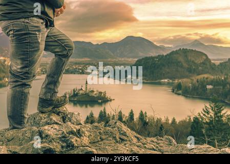 Immagine con le gambe di un turista uomo arrampicato sulle rocce al di sopra del lago di Bled, in Slovenia, guardando la bellissima alba e le Alpi Giulie Foto Stock