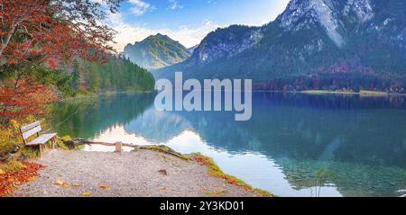 Scenario contemplativa con una panca in legno posto sul lago Alpsee shore, in autunno decor, con la foresta bavarese e montagne si riflette in w Foto Stock