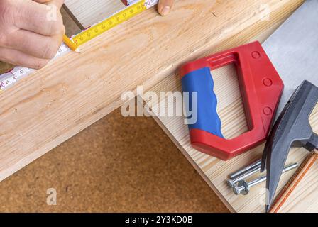 Immagine di sfondo della falegnameria con strumenti per la lavorazione del legno sul tavolo e mani di un uomo che misurano un pannello di legno con metro a nastro e matita Foto Stock