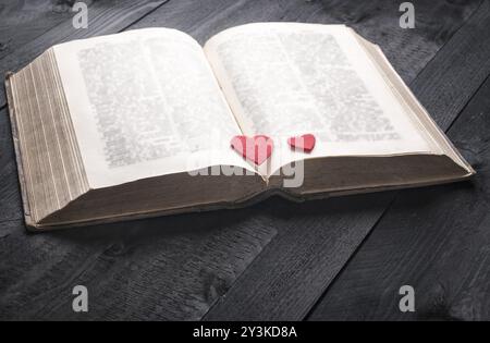 Immagine a tema scolastico con un antico libro aperto e due cuori rossi sulle sue pagine, esposta su un tavolo in legno d'epoca. Un concetto per leggere, studiare Foto Stock