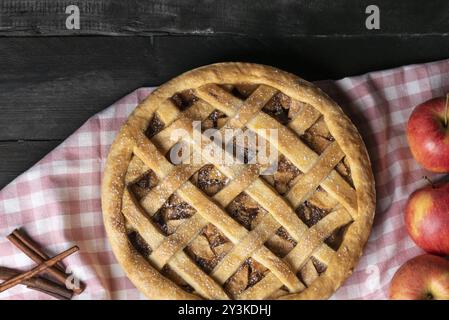 Tavolo rustico con un'intera torta di mele classica su un asciugamano da cucina rosa, circondato da frutta di mele e cannella. Sopra la vista. Dessert fatti in casa Foto Stock