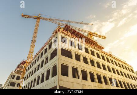 Edificio per uffici in costruzione e le due gru a torre in prossimità di essa, in una giornata di sole Foto Stock