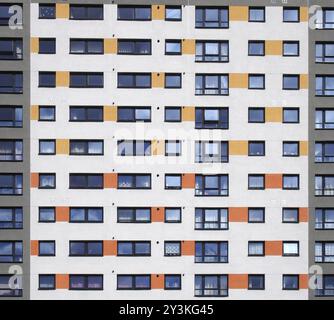 Un'immagine a cornice completa di finestre in un grande e alto edificio di appartamenti con file ripetute di finestre con pareti bianche con dettagli arancioni e grigi Foto Stock