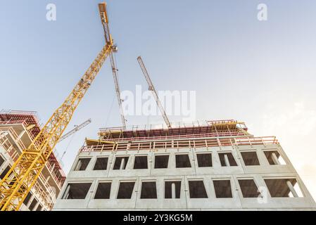 Bottom-up immagine con paio di gru a torre e moderno edificio in costruzione Foto Stock