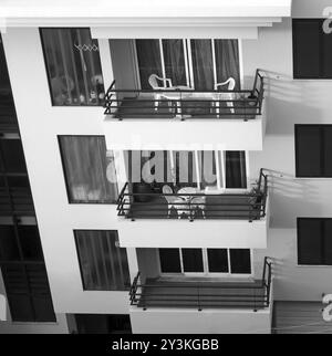 Immagine monocromatica che guarda in basso su una fila di balconi con tavoli e sedie in un condominio in cemento Foto Stock