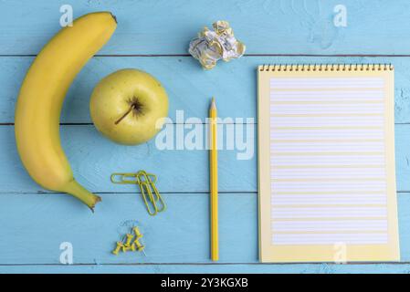 Aprire il notebook e frutta fresca su di un legno blu scrivania in ufficio. Piano immagine di laici con il giallo delle forniture per ufficio e prima colazione Foto Stock