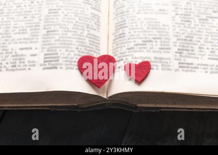 Close-up immagine con due cuori rossi collocato su un vecchio libro aperto, su di un tavolo di legno. Un concetto di lettura, di apprendimento, di educazione o di una storia di amore, roma Foto Stock