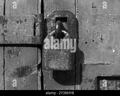 Primo piano monocromatico di un vecchio lucchetto chiuso arrugginito e fibbia su una porta in legno angosciato Foto Stock