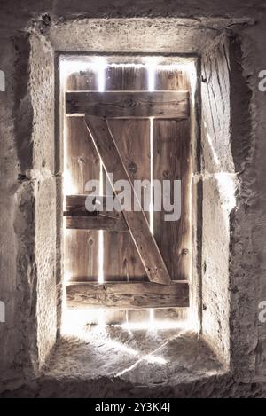 Una forte luce proveniente attraverso le crepe da una vecchia porta di legno Foto Stock