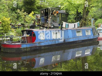 Un'antica barca blu sgarbata ormeggiata accanto a capannoni di legno con lavaggio sulla linea sul canale rochdale vicino al ponte hebden Foto Stock