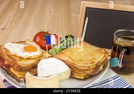 Colazione francese specifica con panini al formaggio fuso, formaggio bianco con bandiera francese, insalata, tazza di tè e lavagna bianca, su un tavolo di legno Foto Stock