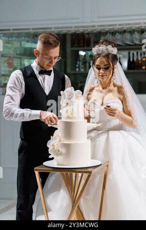 Elegante cerimonia nuziale con happy pair che prepara una torta a strati splendidamente decorata. Foto Stock