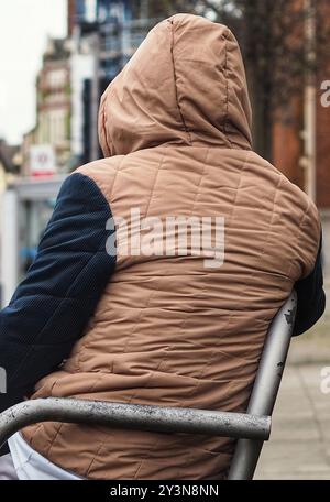 Vista posteriore di un giovane uomo seduto, che indossa una felpa con cappuccio e parla sul suo cellulare - febbraio 2024 Foto Stock