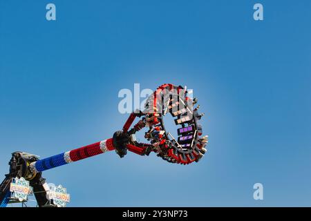 Un emozionante giro nel parco divertimenti con una piattaforma circolare con posti a sedere per i motociclisti, sospesi in aria contro un cielo azzurro. La corsa è decora Foto Stock