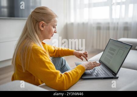 Una donna bionda lavora con molta attenzione dal suo ufficio domestico, scrivendo su un notebook Foto Stock
