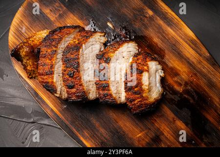 Maiale cotto tagliato a pezzi su un asse di legno su un tavolo grigio. Foto di alta qualità Foto Stock