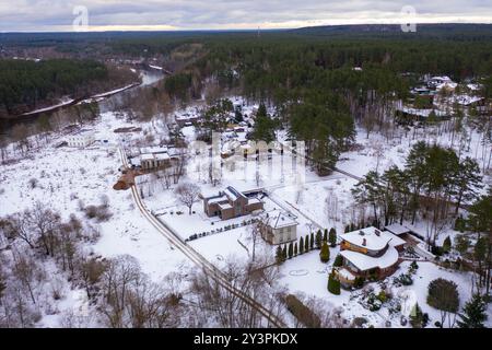 Vista aerea di un paesaggio innevato caratterizzato da diversi edifici circondati da alberi. La scena comprende un mix di strutture residenziali con tetti rossi, p Foto Stock