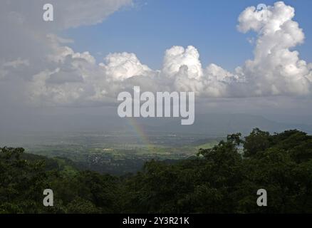 Un arcobaleno si forma vicino alla città di Neral sotto della stazione collinare di Matheran nel distretto di Raigad alla periferia di Mumbai. Matheran è una splendida stazione collinare situata alla periferia della città nel quartiere Raigad di Maharashtra. i veicoli a motore sono vietati nella stazione della collina e i turisti possono prendere un treno giocattolo che va proprio all'interno della stazione della collina da dove i turisti possono camminare o noleggiare un risciò trainato a mano o andare a cavallo per visite turistiche all'interno e intorno alla stazione della collina. i mesi monsonici sono preferiti dai turisti in quanto l'intera stazione collinare si trasforma in un tappeto verde a causa della pioggia. Foto Stock