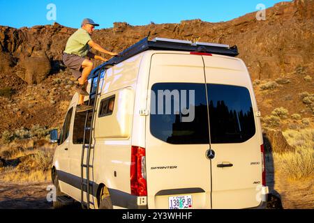 Un singolo maschio senior sale una scala fino alla cima del furgone velocista Mercedes Benze nell'area di arrampicata di Coulee. Vantage, Washington Foto Stock