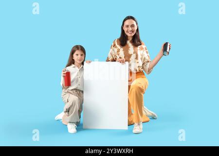 La bambina e sua madre hanno in mano bombolette di vernice spray con carta bianca su sfondo blu Foto Stock