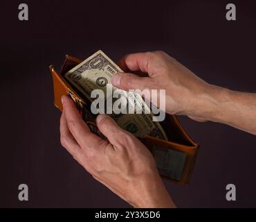 Le mani di un uomo tengono aperto un vecchio portafoglio a un solo dollaro Foto Stock