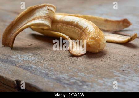 metà sbucciato su banane mature con polpa cremosa esposta sulla superficie del tavolo, quasi marcio o rovinato, frutta poco attraente a fuoco selettivo con copia Foto Stock