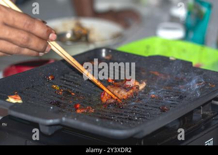 Grigliare le mani con le bacchette. Gli uomini girano la carne con le bacchette su una padella. Foto Stock