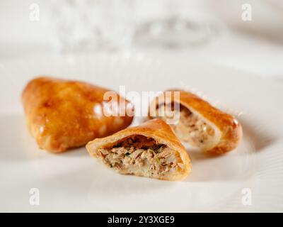 Piccole torte russe con tonno macinato Russian Piroshki. Pesce di tonno cotto torte fatte a mano o empanadas tagliate a metà su piatto bianco nell'elegante interno del ristorante. Messa a fuoco selettiva, primo piano. Foto Stock