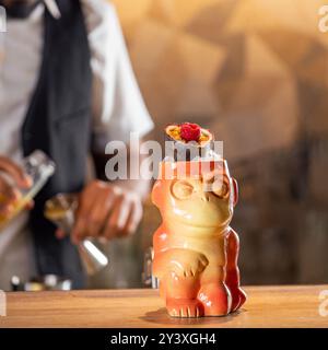 Tiki drink cocktail. Un cocktail tropicale tiki al bancone del bar. Cocktail Tiki in tazza di scimmia decorata con fichi e lamponi al bar nel night club Foto Stock