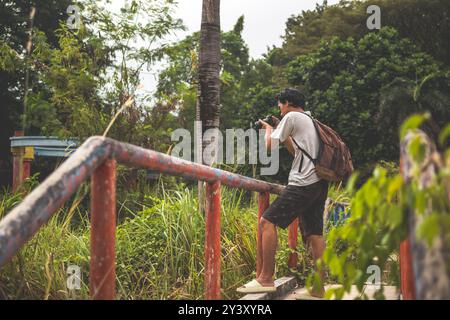 Gli uomini cercano di scattare foto da un parco abbandonato con la macchina fotografica in mano. Zaino in spalla solo in piedi sul bordo del ponte per scattare foto. Foto Stock