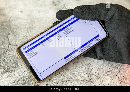 Londra. REGNO UNITO- 09.12.2024. Un lavoratore che indossa guanti da lavoro e tiene in mano un cellulare con uno stipendio digitale. Foto Stock