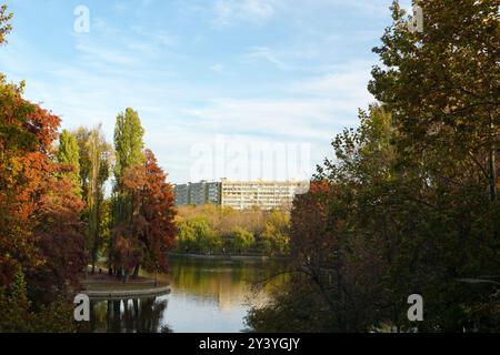 Splendido paesaggio autunnale con alberi, lago e blocco di appartamenti nel parco IOR nel quartiere Titan a Bucarest, Romania Foto Stock