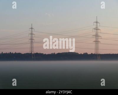 ...der Herbst ist endgueltig in unseren Landen angekommen - Die fruehen Nebel weben ihr seidenes Gewand...und aus den Wiesen um die Energiemasten steiget... Energie im Fruehnebel **** l'autunno è finalmente arrivato nelle nostre terre, le prime nebbie tessono le loro vesti di seta e l'energia sale dai prati intorno agli alberi di energia nella nebbia di prima mattina Foto Stock