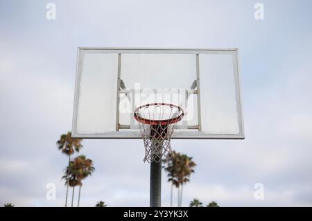 Un primo piano di un canestro da basket all'aperto con un pannello posteriore in vetro trasparente, sullo sfondo di un cielo luminoso di giorno. Foto Stock