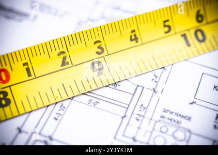 Vista ravvicinata di un metro a nastro giallo posizionato su intricati progetti architettonici, che enfatizza la precisione e l'attenzione ai dettagli nei costrutti Foto Stock