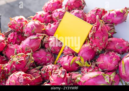 Frutta di drago dai colori vivaci impilata in un mercato con un cartello giallo che indica il prezzo Foto Stock